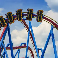 Wagoniki najwyższego rollercoastera na świecie pędzą po czerwono-żółtych torach na tle błękitnego nieba z chmurami.