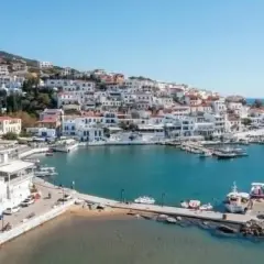 Malowniczy port na wyspie Andros, z białymi domkami wznoszącymi się na wzgórzu i błękitnym morzem.