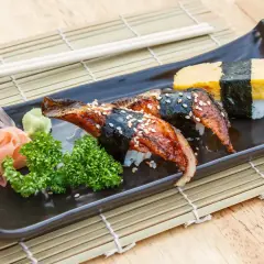 Wyśmienite unagi sushi z sezamem, podane z wasabi, imbirem i natką pietruszki na czarnej tacce.