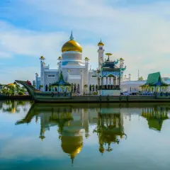 Złota kopuła meczetu Omar Ali Saifuddien w Brunei odbija się w spokojnej wodzie. Obok unosi się ozdobna łódź.