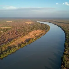 Szeroka rzeka Niger meandruje przez sawannę, otoczona bujną roślinnością i nielicznymi osadami.