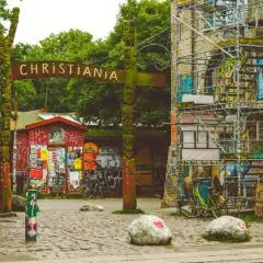 Drewniany totem i tablica z napisem CHRISTIANIA witają w wolnym mieście. Kolorowe budynki i rowery tworzą niepowtarzalny klimat.