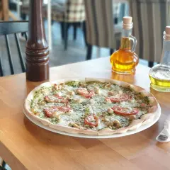 Pyszna pizza z kurczakiem i pomidorami, idealna dla szukających bezglutenowych restauracji. Na stole oliwa i przyprawnik.
