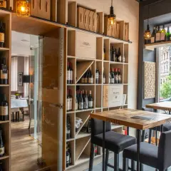 Wnętrze restauracji Muga z regałami pełnymi win, drewnianymi stołami i krzesłami barowymi.