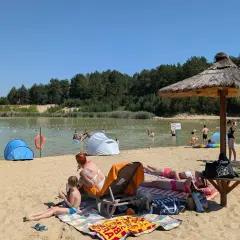 Słoneczny dzień nad zalewem Biszcza. Ludzie opalają się na plaży, kąpią w wodzie i odpoczywają pod parasolami.