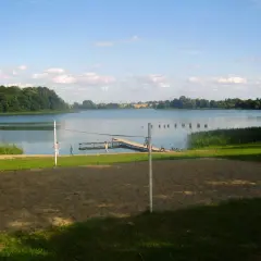 Piękny dzień nad jeziorem Skiertąg. Piaskowa plaża, pomost i zielone drzewa tworzą sielski krajobraz.