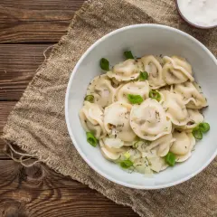 Pyszne pierogi z cebulką i koperkiem, idealne na obiad w stylu zapiecek warszawa. Obok miseczka śmietany i widelec.