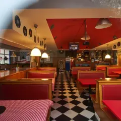 Wnętrze w stylu retro z czerwonymi kanapami i czarno-białą podłogą w szachownicę. W tle widać jukebox i dekoracje z płyt winylowych, idealne dla Queens Street Bar.