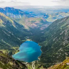 Widok z góry na Morskie Oko, jakby z kamery na żywo. Turkusowa tafla jeziora otoczona zielonymi zboczami Tatr.
