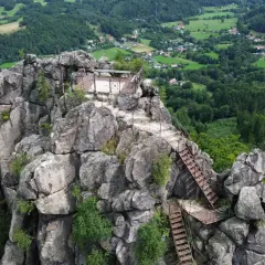 Widok z góry na skalne miasto Sokolik Duży, z metalowymi schodami prowadzącymi na szczyt. W dole rozciąga się zielona dolina z domkami.
