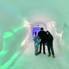 Rodzina w lodowym tunelu, który wygląda jak wejście do wioski Świętego Mikołaja. Ściany są oświetlone na zielono.