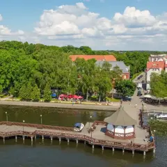 Malownicze miejscowości na Mazurach: drewniane molo z altaną, zielony park i urokliwe kamienice nad jeziorem.