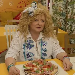Kobieta z kręconymi włosami siedzi przy stoliku w bistro. Przed nią pizza, a za nią dekoracje ścienne. To idealne miejsce na bistro schadzka przy piecu.