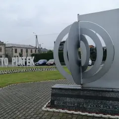 Geometryczny środek Polski w miejscowości Piątek. Monumentalna rzeźba i napis "Miasto Piątek" na tle budynków.