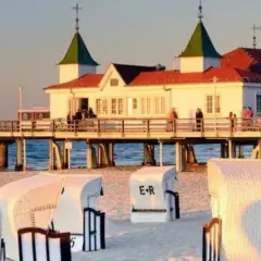 Zachód słońca nad molo w Ahlbecku. Białe kosze plażowe na piasku, a w tle budynek z restauracją i niemiecką flagą. To jedne z wielu atrakcji Ahlbecku.