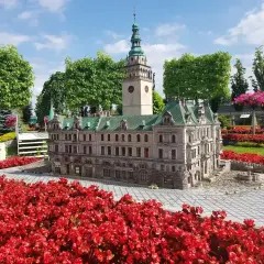 Miniatura ratusza z wieżą zegarową, otoczona czerwonymi kwiatami, w miniaturowej Kotlinie Kłodzkiej.