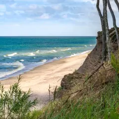 Spokojne miejsca nad morzem: piaszczysta plaża, turkusowe fale i klif porośnięty drzewami. Idealne na relaks.