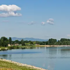 Spokojne otmuchów jezioro z łodziami przy brzegu, otoczone zielonymi drzewami i górami w tle.