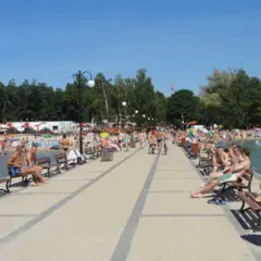 Ludzie odpoczywają na pomoście nad Skorzęcinem, jezioro tętni życiem, plaża pełna plażowiczów.