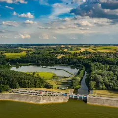 Malowniczy krajobraz z tamą i zbiornikiem wodnym. Jezioro Chańcza otoczone lasami i polami, z widoczną drogą na koronie zapory.