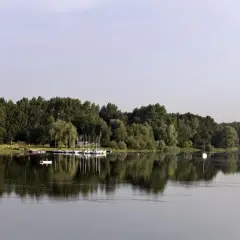 Zalew Przeczyce z łodziami przy brzegu i samotną białą żaglówką na spokojnej tafli wody.