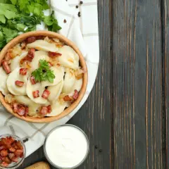 Pyszne pierogi z boczkiem i cebulką, serwowane w drewnianej misie. To kwintesencja kuchni łemkowskiej, podane z kwaśną śmietaną i świeżą natką pietruszki.