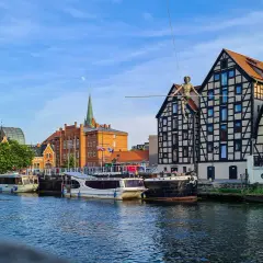 Bydgoszcz wydarzenia dzisiaj: na Wyspie Młyńskiej spaceruje po linie figura, cumują statki, a w tle widać zabytkowe kamienice i nowoczesną architekturę.