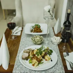 Elegancka kolacja we dwoje w Opolu. Dwa talerze z wykwintnym jedzeniem, kieliszki z czerwonym winem i świece tworzą romantyczny nastrój. Idealne opole atrakcje dla par.