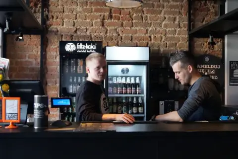 Pracownicy w Bobby Burger Bydgoszcz za ladą, obok lodówki z napojami i ekspresu do kawy.