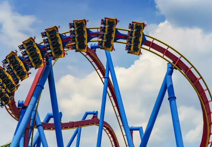 Wagoniki najwyższego rollercoastera na świecie pędzą po czerwono-żółtych torach na tle błękitnego nieba z chmurami.