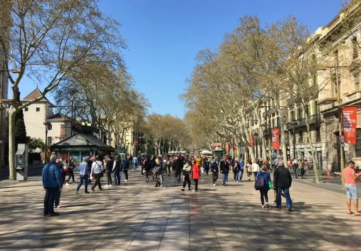 Tłum ludzi spaceruje po La Rambla w Barcelonie, pod cienistymi drzewami i wzdłuż zabytkowych budynków.