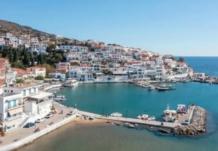 Malowniczy port na wyspie Andros, z białymi domkami wznoszącymi się na wzgórzu i błękitnym morzem.