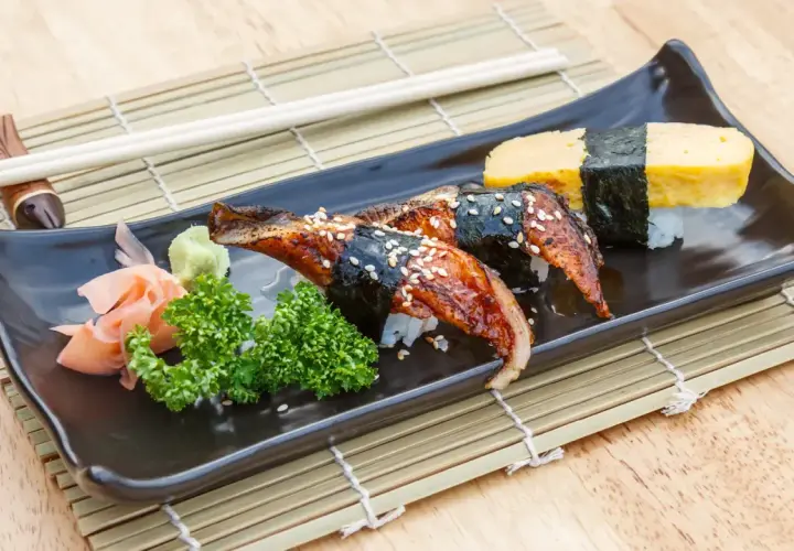 Wyśmienite unagi sushi z sezamem, podane z wasabi, imbirem i natką pietruszki na czarnej tacce.