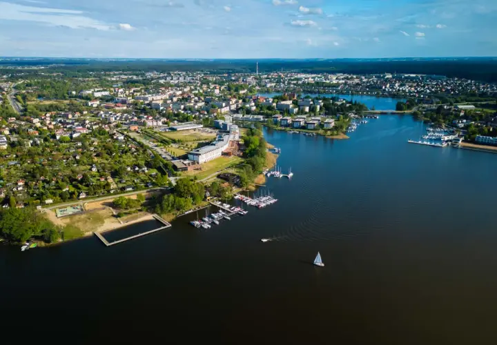 Malownicze miasto nad Jeziorakiem, z mariną pełną żaglówek i łodzi, otoczone zielenią i zabudową mieszkalną.