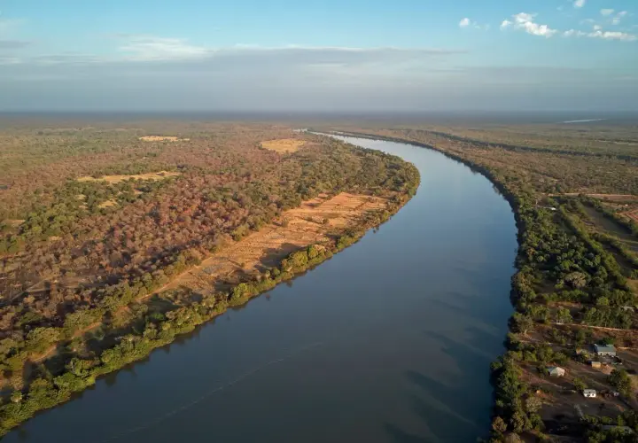 Szeroka rzeka Niger meandruje przez sawannę, otoczona bujną roślinnością i nielicznymi osadami.