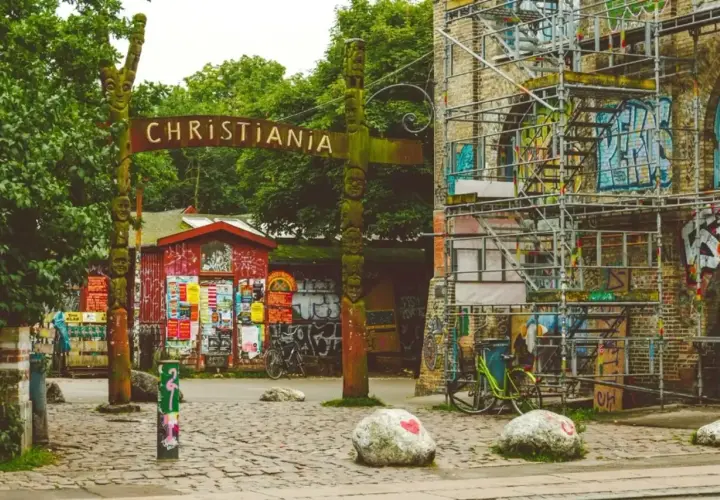 Drewniany totem i tablica z napisem CHRISTIANIA witają w wolnym mieście. Kolorowe budynki i rowery tworzą niepowtarzalny klimat.