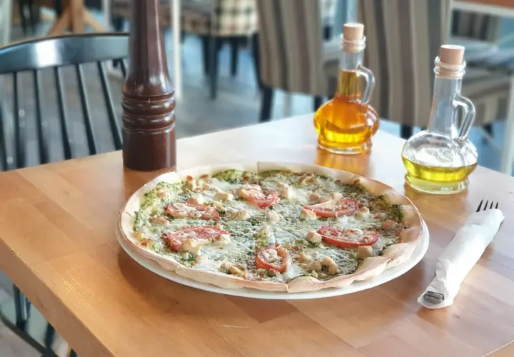 Pyszna pizza z kurczakiem i pomidorami, idealna dla szukających bezglutenowych restauracji. Na stole oliwa i przyprawnik.