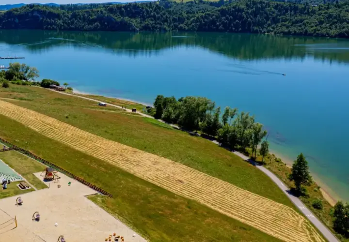 Malownicze jezioro czorsztyńskie z widokiem na domki, plac zabaw i plażę. Idealne miejsce na wypoczynek i odkrywanie atrakcji.