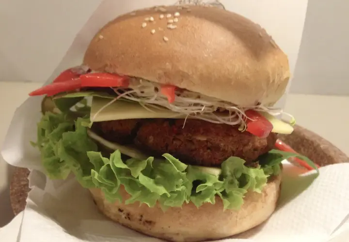 Pyszny burger z Krowarzywa Kraków: soczysty kotlet roślinny, świeża sałata, ser, pomidor i kiełki w miękkiej bułce.