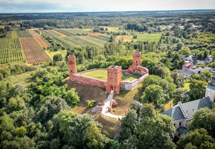 Ruiny zamku w krajobrazie rolniczym, otoczone lasem. To malownicze miejsce znajduje się w województwie mazowieckim, największym województwie w Polsce.