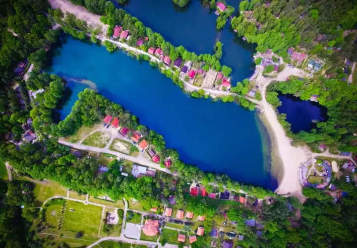Malownicze rokitki jezioro otoczone lasem i domkami z czerwonymi dachami. Woda lśni błękitem, a plaża zaprasza do odpoczynku.
