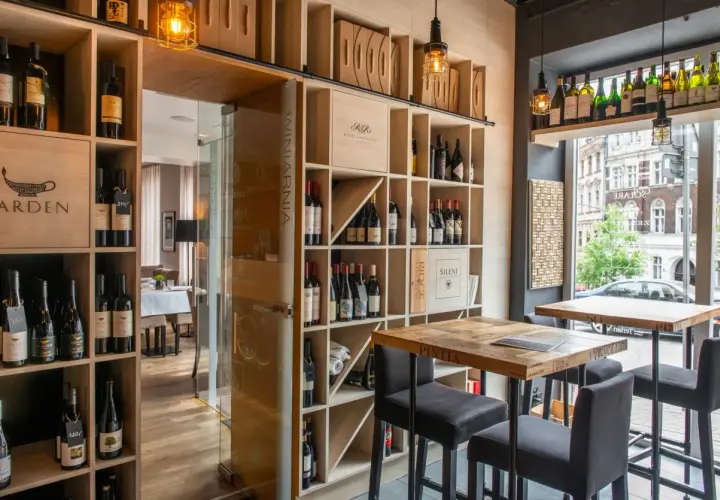 Wnętrze restauracji Muga z regałami pełnymi win, drewnianymi stołami i krzesłami barowymi.