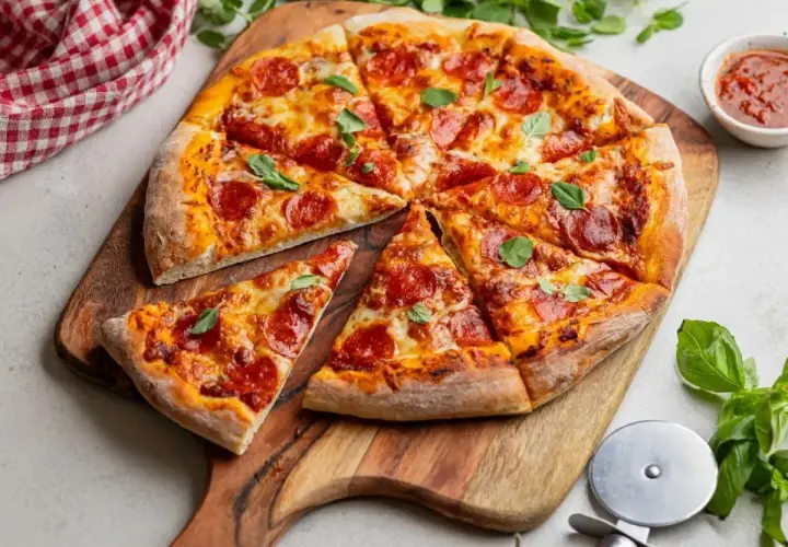 Pyszna pizza z peperoni, ciągnącym serem i świeżą bazylią, pokrojona na kawałki na drewnianej desce.