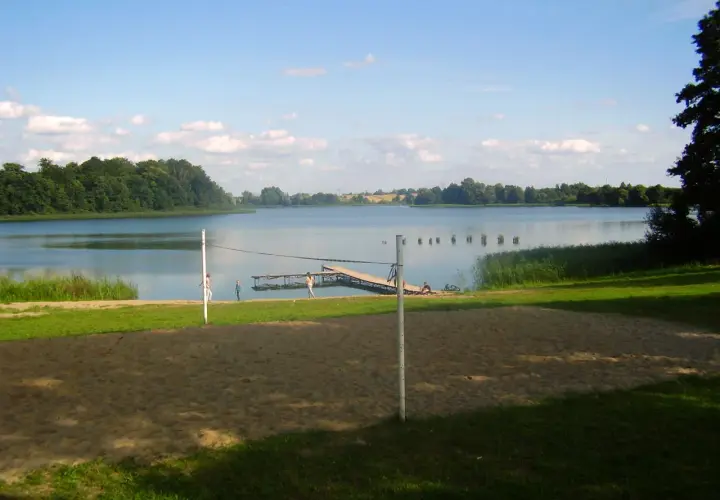 Piękny dzień nad jeziorem Skiertąg. Piaskowa plaża, pomost i zielone drzewa tworzą sielski krajobraz.