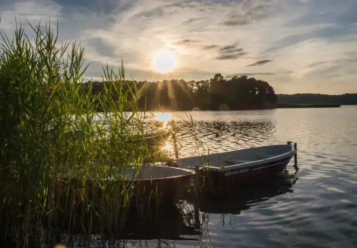 Dwa łodzie przy brzegu jeziora Świętajno, w blasku zachodzącego słońca.