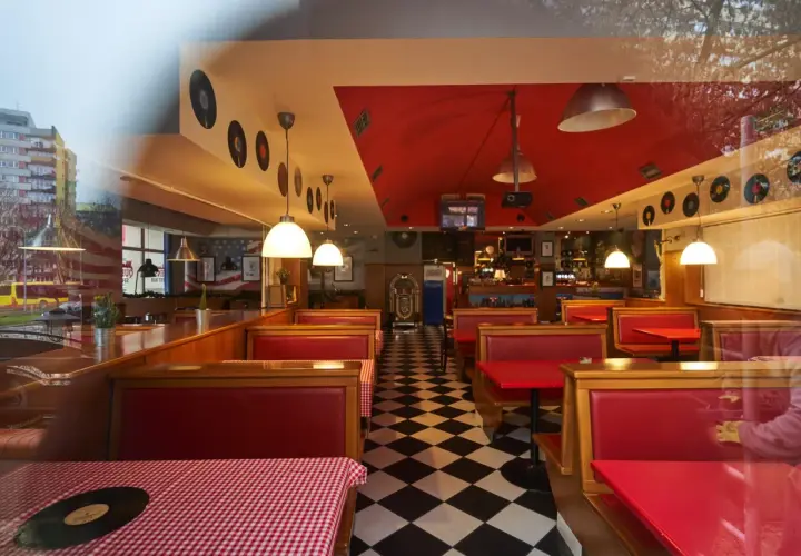Wnętrze w stylu retro z czerwonymi kanapami i czarno-białą podłogą w szachownicę. W tle widać jukebox i dekoracje z płyt winylowych, idealne dla Queens Street Bar.