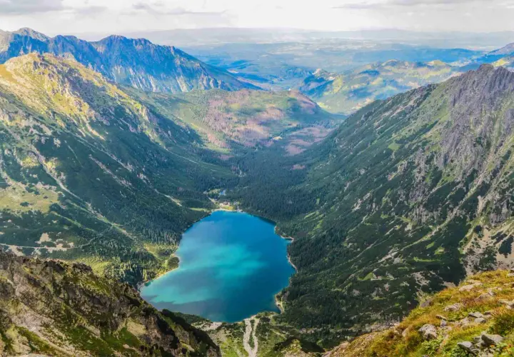 Widok z góry na Morskie Oko, jakby z kamery na żywo. Turkusowa tafla jeziora otoczona zielonymi zboczami Tatr.