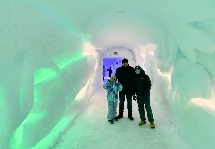 Rodzina w lodowym tunelu, który wygląda jak wejście do wioski Świętego Mikołaja. Ściany są oświetlone na zielono.