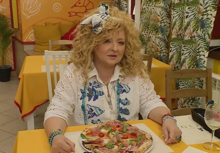 Kobieta z kręconymi włosami siedzi przy stoliku w bistro. Przed nią pizza, a za nią dekoracje ścienne. To idealne miejsce na bistro schadzka przy piecu.