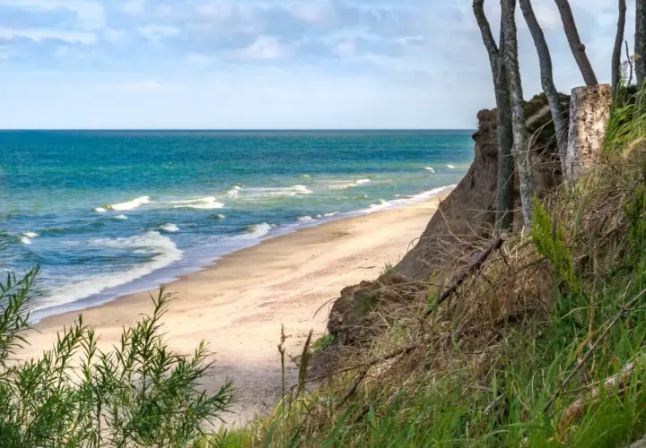 Spokojne miejsca nad morzem: piaszczysta plaża, turkusowe fale i klif porośnięty drzewami. Idealne na relaks.